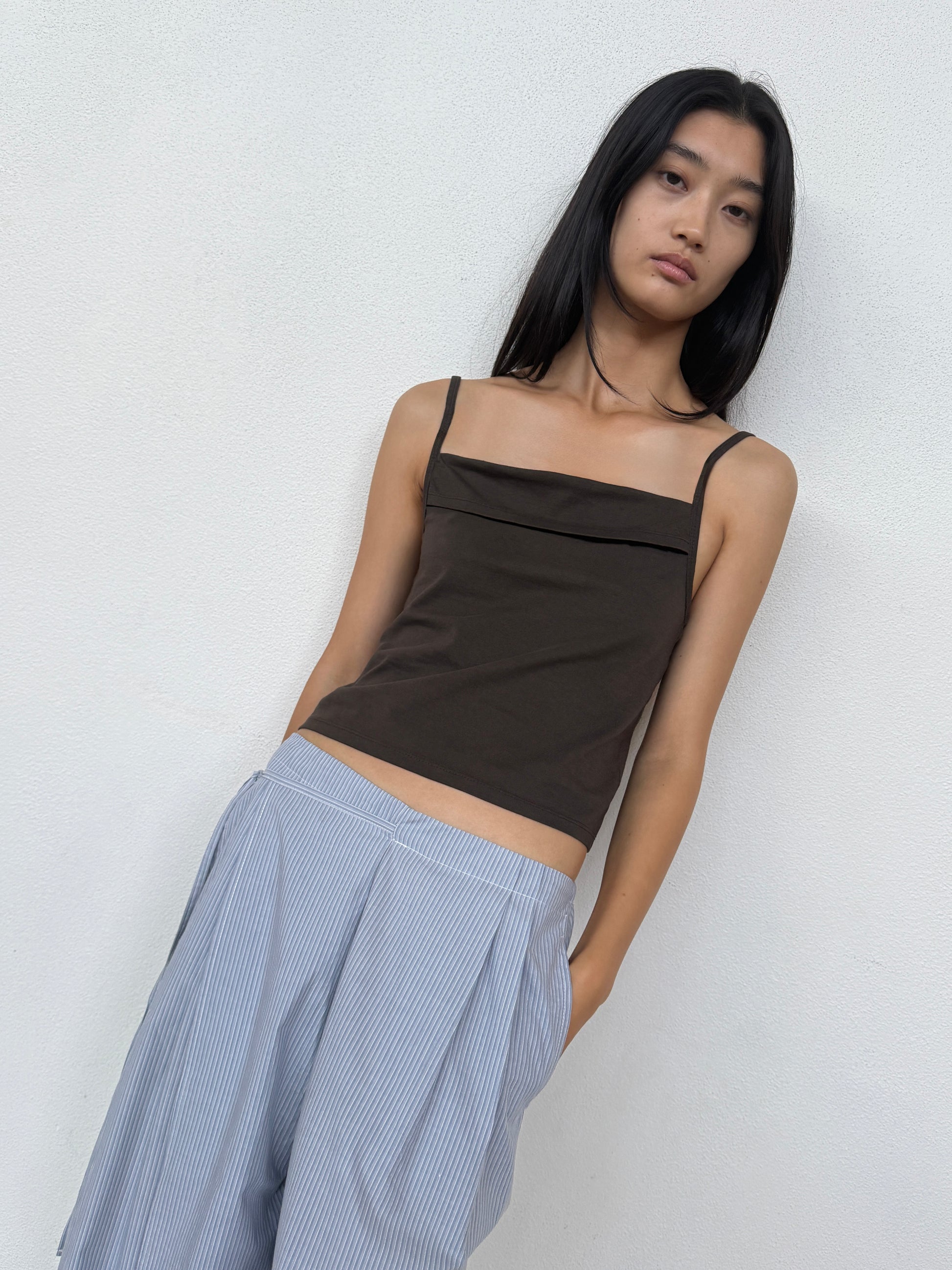A person with long dark hair wears the 0 Double Layer Pant - Sky Stripe and a sleeveless brown top, standing against a plain white wall and looking at the camera.