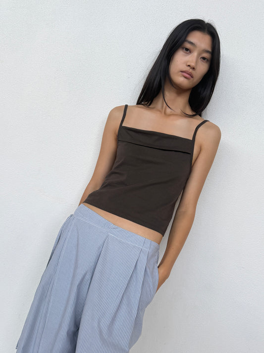 A person with long dark hair wears the 0 Double Layer Pant - Sky Stripe and a sleeveless brown top, standing against a plain white wall and looking at the camera.