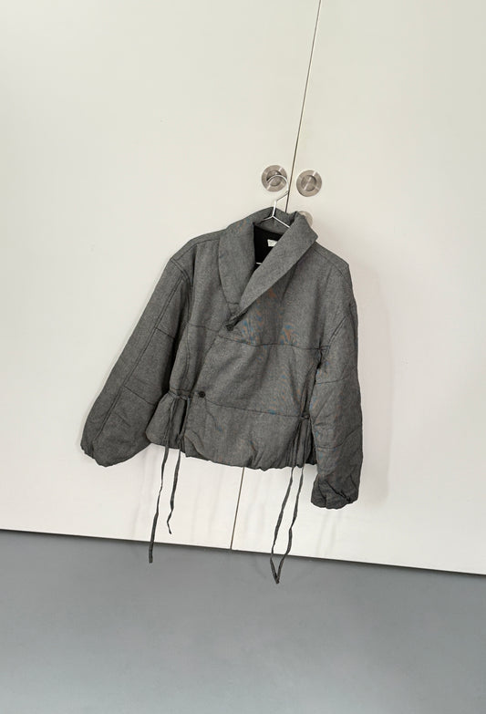 The Exclusive Bubble Coat - Black White Stripe by 0, featuring a relaxed fit and soft, quilted organic cotton, hangs on silver knobs against a white door. It has a high collar and drawstrings, and showcases distinctive black and white stripes.