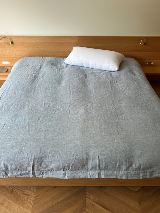 A neatly made bed features the Duvet cover - Blue Stripe and a single white pillow, set against a wooden headboard with built-in reading lights on a wooden floor. Hypo-allergenic bedding ensures comfort and peace of mind.