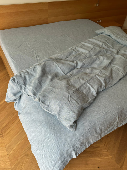 A bed features the Duvet cover - Blue Stripe and matching comforter, partially folded back to reveal the mattress. The headboard is wooden, and the floor displays a light brown wood pattern.