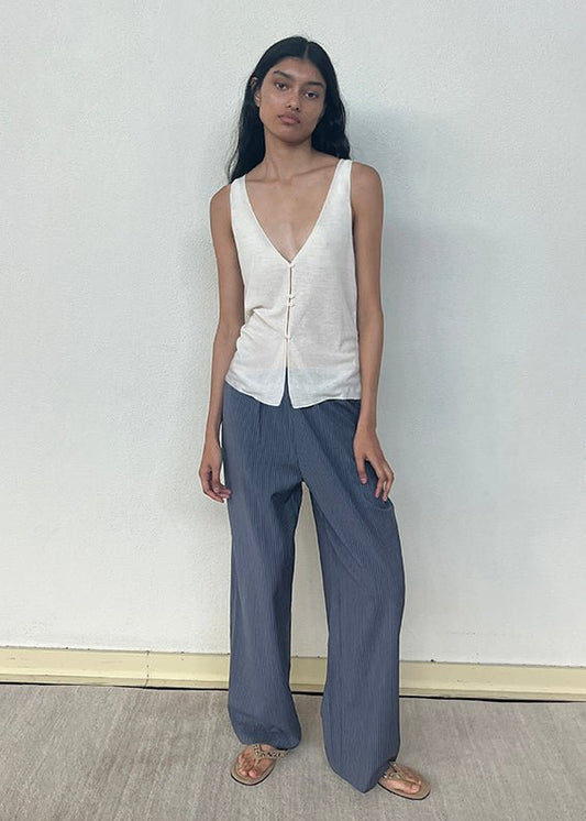 A model wears the Button Up Knit Tank - Off White by Deiji Studios, crafted from recycled polyester, styled with wide-leg grey striped trousers and tan flat sandals, standing against a white wall.