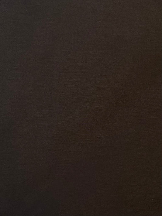 A close-up of the Press Stud Saddle Bag in Dark Chocolate shows a richly textured, dark brown surface with subtle shading, echoing sculptural elements of premium design.