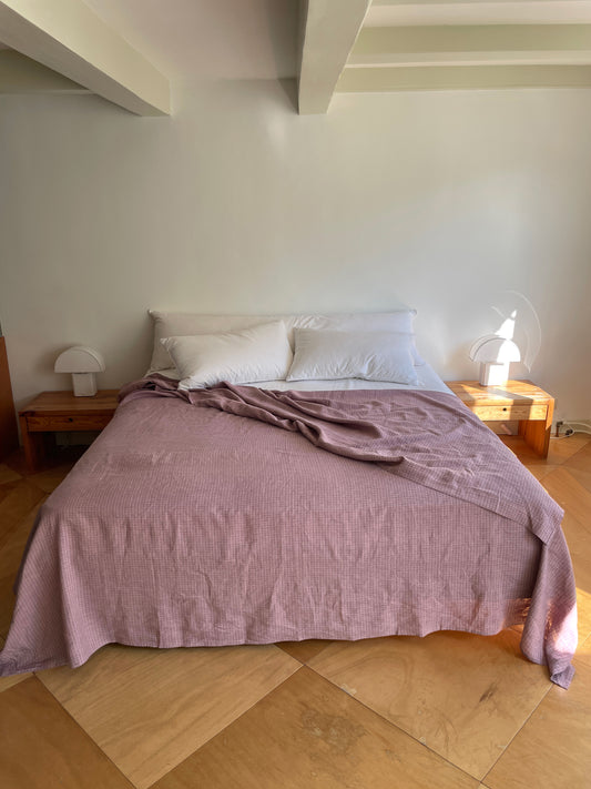 A neatly made bed with white pillows and Sheets - Musk Check sits against a white wall, flanked by wooden nightstands and modern lamps, in a sunlit room with light wood floors.