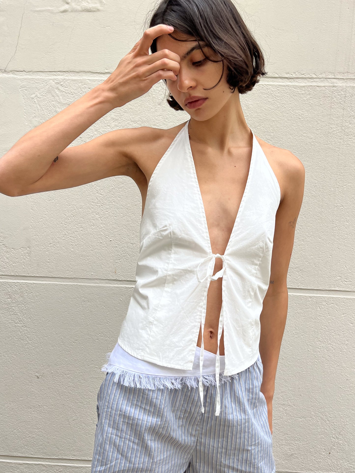 female model wears the open halter top top by Deiji Studios in white
top features open front with centre bust tie, halter neck tie and v neckline, bust seams for subtle shaping and shirred back
made from 100% GOTS certified organic cotton poplin
paired with a blue stripe cotton short