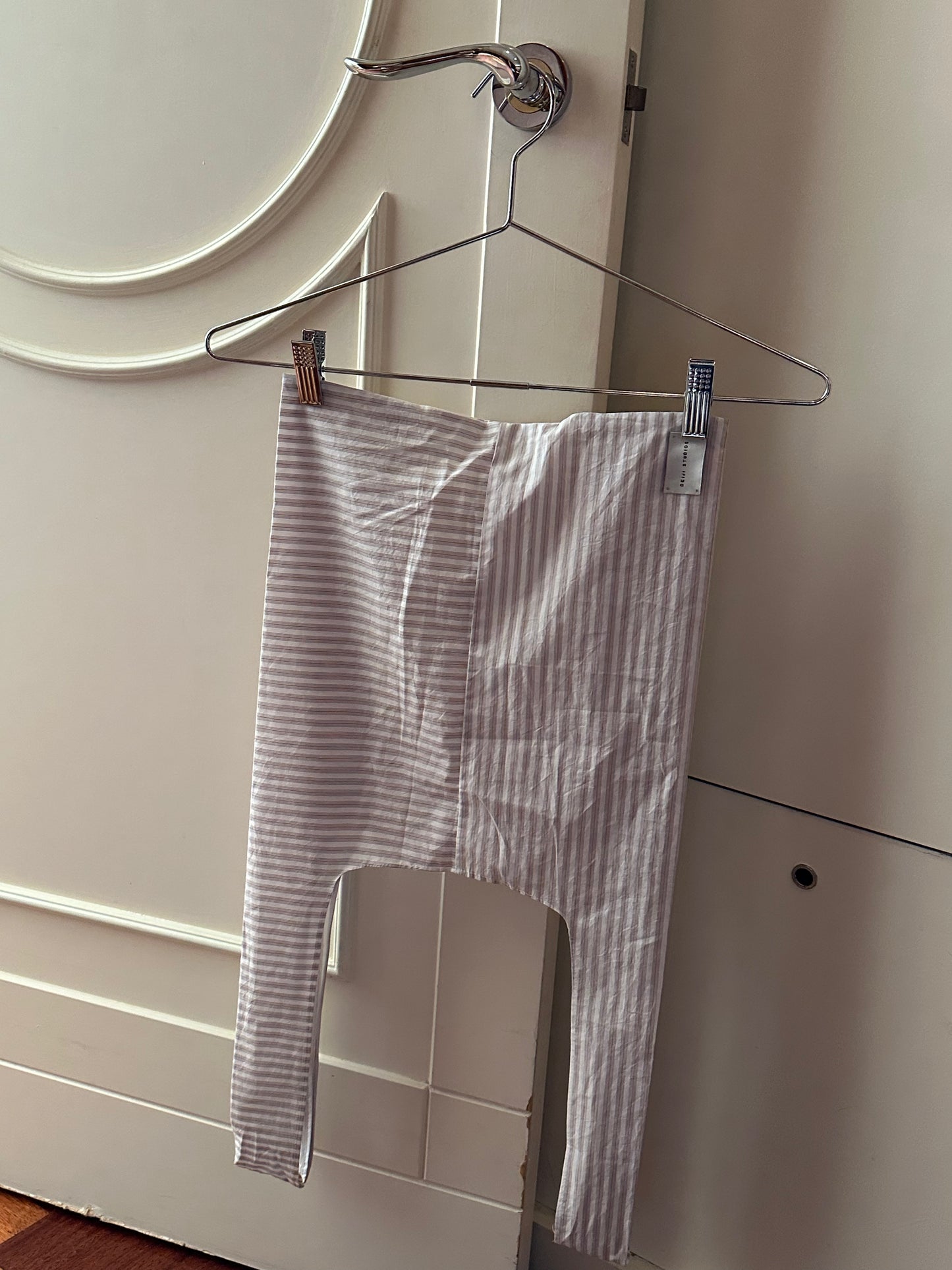 A Seam Tote in Lake Stripe from Deiji Studios hangs from a metal hanger on a door handle in a softly lit room.