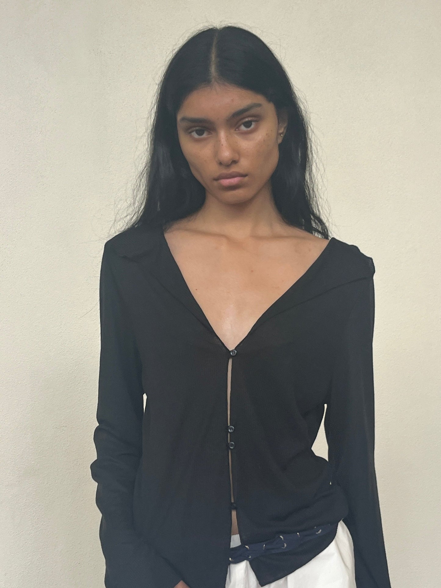 A person with long dark hair wears the Open Long Sleeve Top in black with an open neckline and white pants, standing against a plain light-colored background.