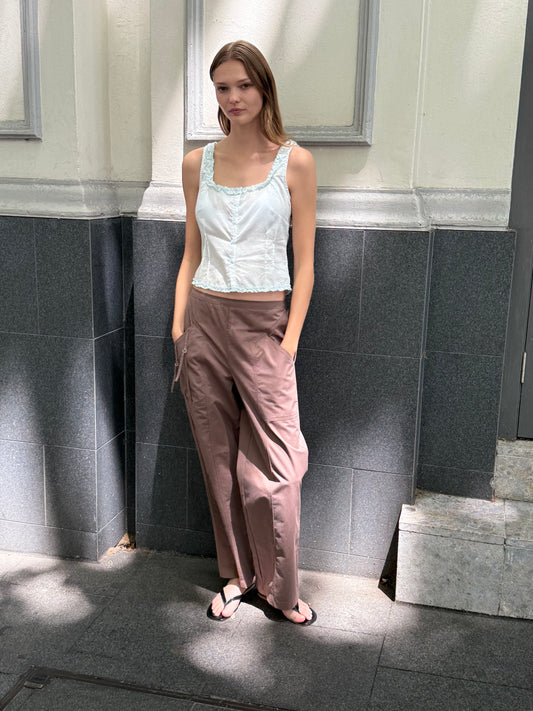 A model wears the Button Frill Top - Mint by Deiji Studios with wide-leg mauve cargo trousers and black sandals, standing against an outdoor grey tiled wall.
