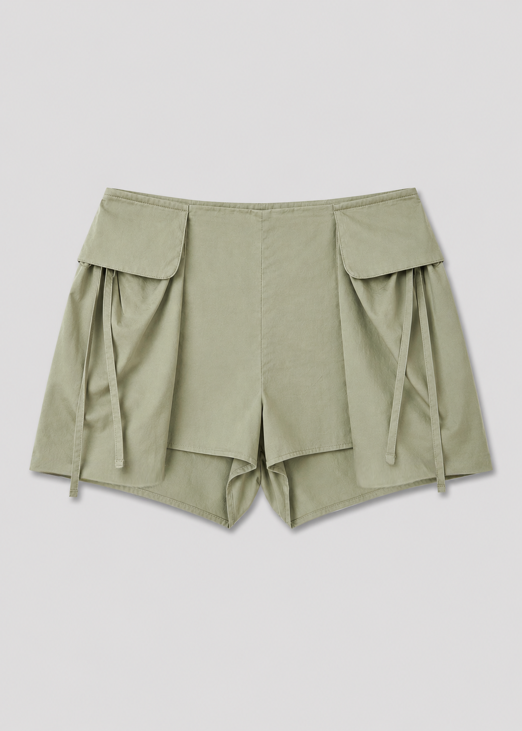 The Micro Pocket Short - Stone Green by Deiji Studios, with large front flap pockets and decorative side ties, is displayed laid flat on a white background.