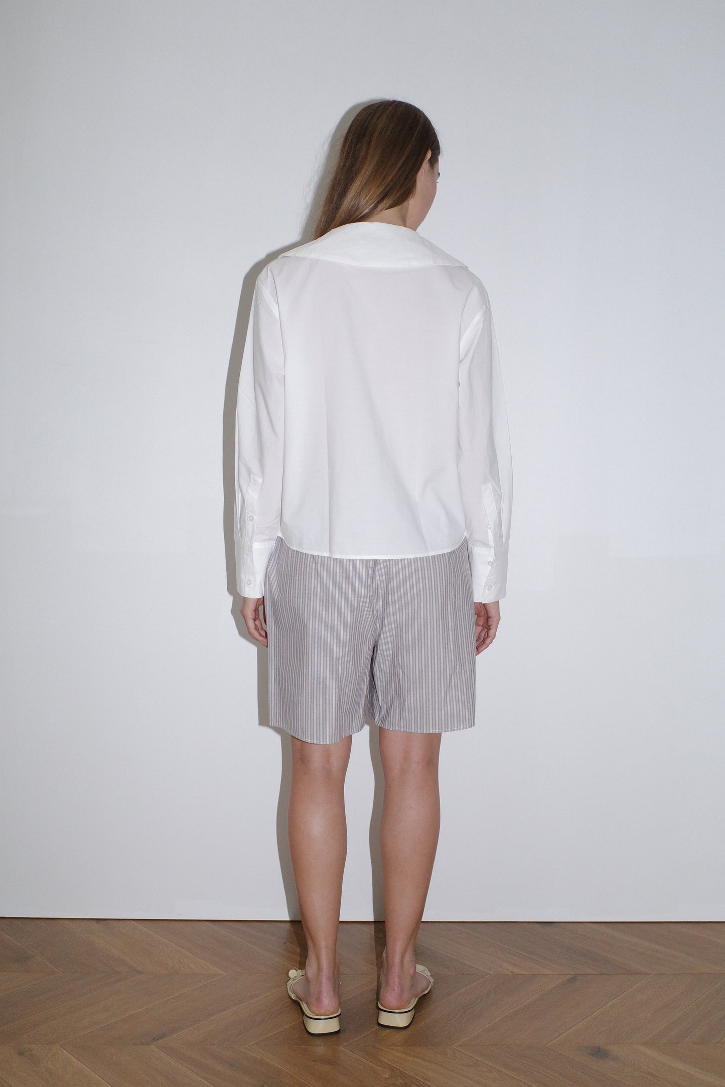 female model wears the collared tie shirt by Deiji Studios in white
a structured shirt features an oversized collar and cuff, tie at front collar opening, dropped shoulder and elongated sleeves in a boxy fit
made from 100% GOTS certified organic cotton poplin
paired with a blue stripe boxer short