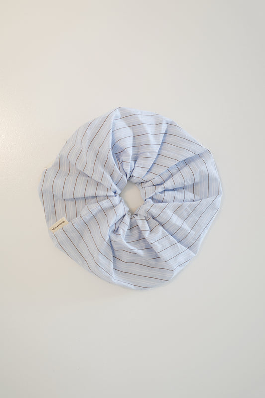 The Scrunchie - Mineral Stripe is a voluminous, oversized light blue cotton scrunchie with brown pinstripes, a gathered circular design, and a small Deiji Studios branded label, shown laid flat on a white surface.
