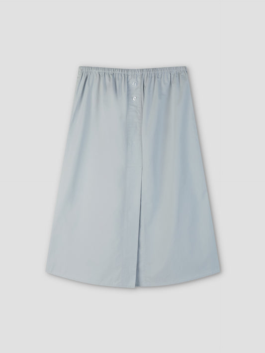 The Overlap Skirt - Blue by Deiji Studios is a light blue, knee-length A-line skirt with an elastic waistband and front button detail, shown on a plain light gray background.