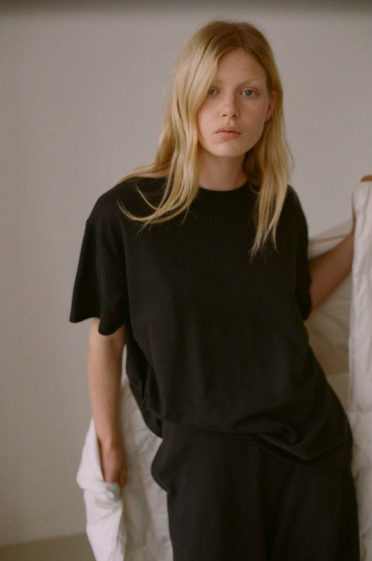 Female model wearing the leisure tee - black by Deiji Studios against plain background