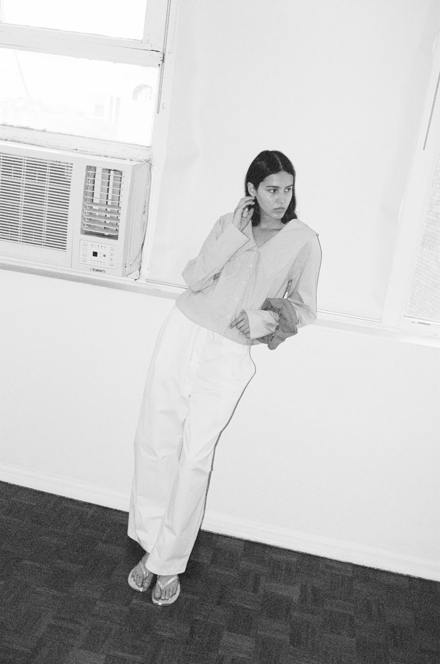 high angle shot of a female model wearing white Deiji Studios cotton twill pants, features a drawcord waist and relaxed leg in a full length. Styled with the Deiji Studios oversized collared shirt in light blue Dream Stripe, features a button front and oversized pointed collar
