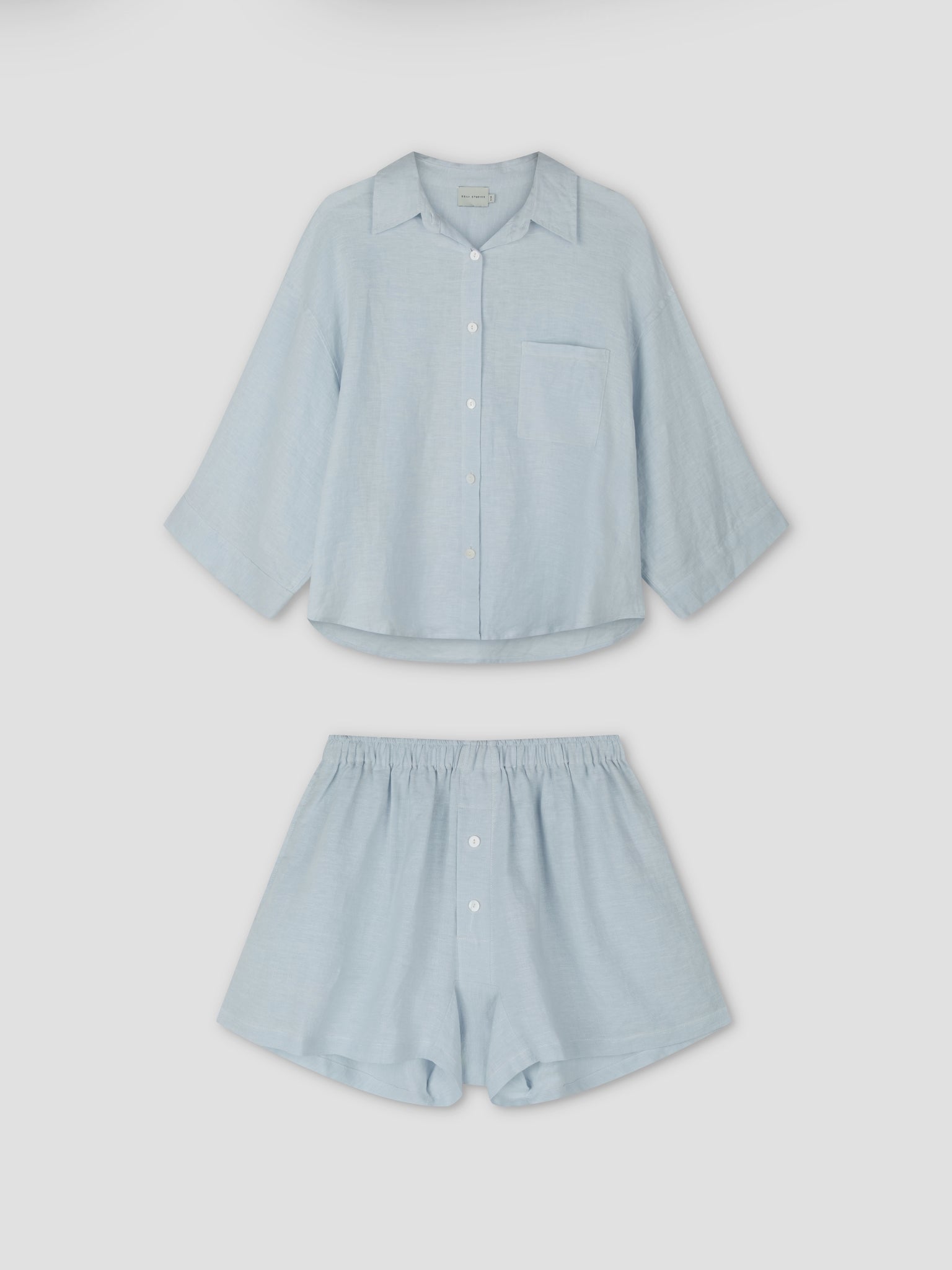 The 03 Set - Soft Blue by Deiji Studios features an oversized light blue linen shirt with a chest pocket and matching boxer-style shorts with front buttons, shown on a plain white background.