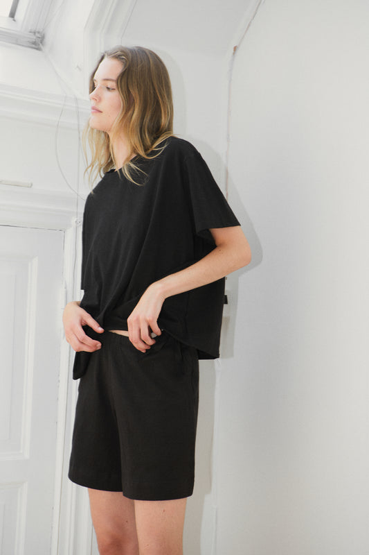 Female model wearing the leisure tee - black by Deiji Studios against plain background