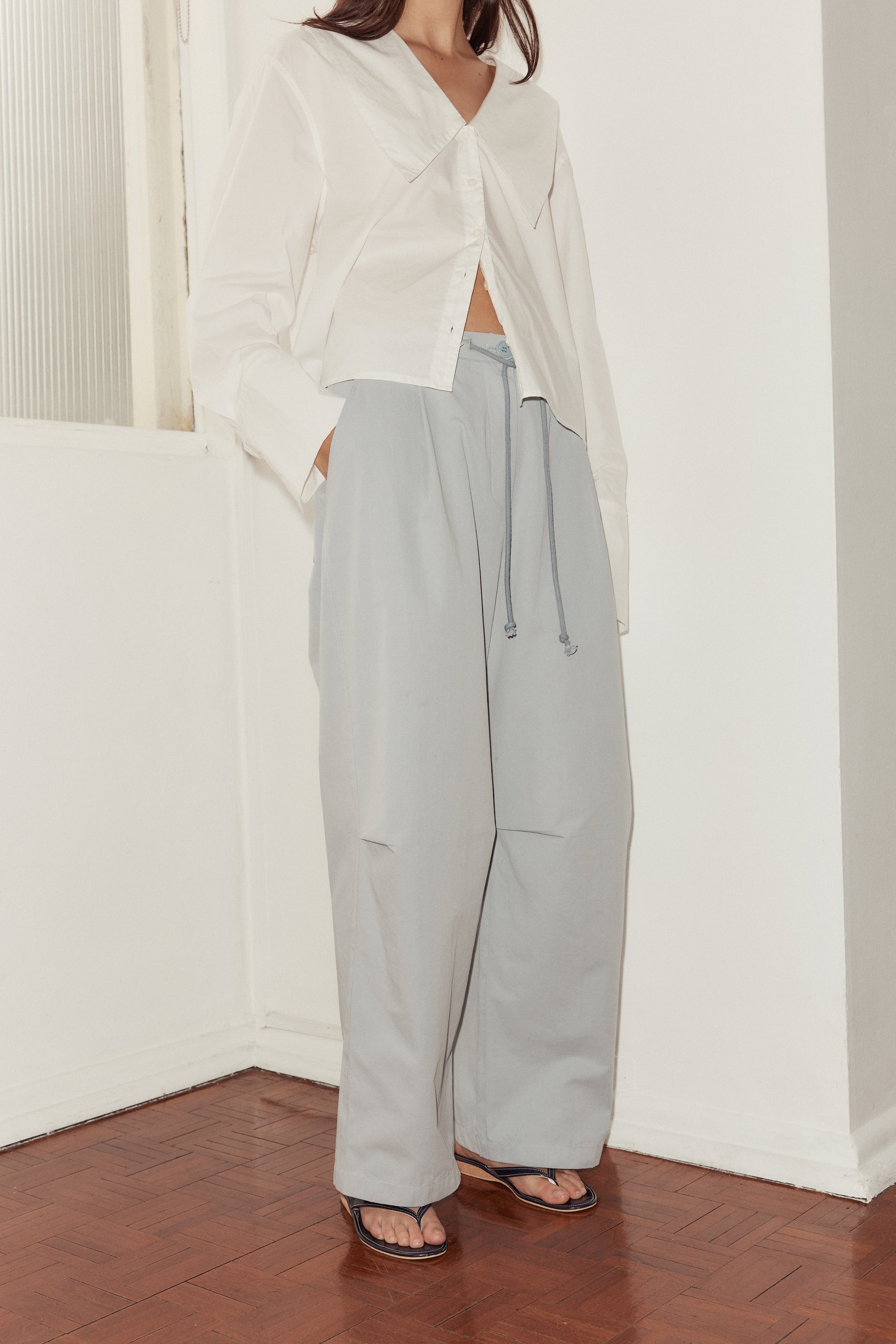 mid shot female model Deiji Studios sky blue cotton twill pants, with a relaxed fit, tucks at the knee and drawcord waist.