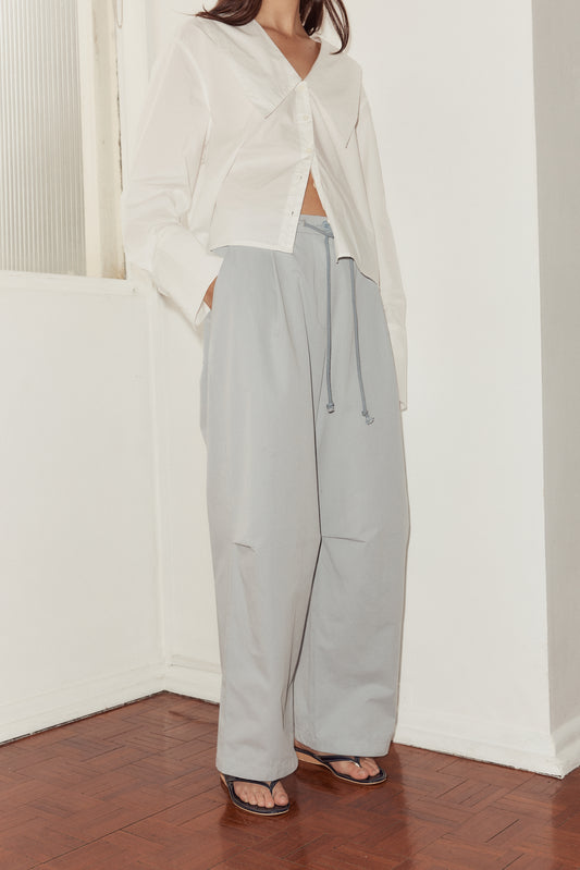 mid shot female model Deiji Studios sky blue cotton twill pants, with a relaxed fit, tucks at the knee and drawcord waist.