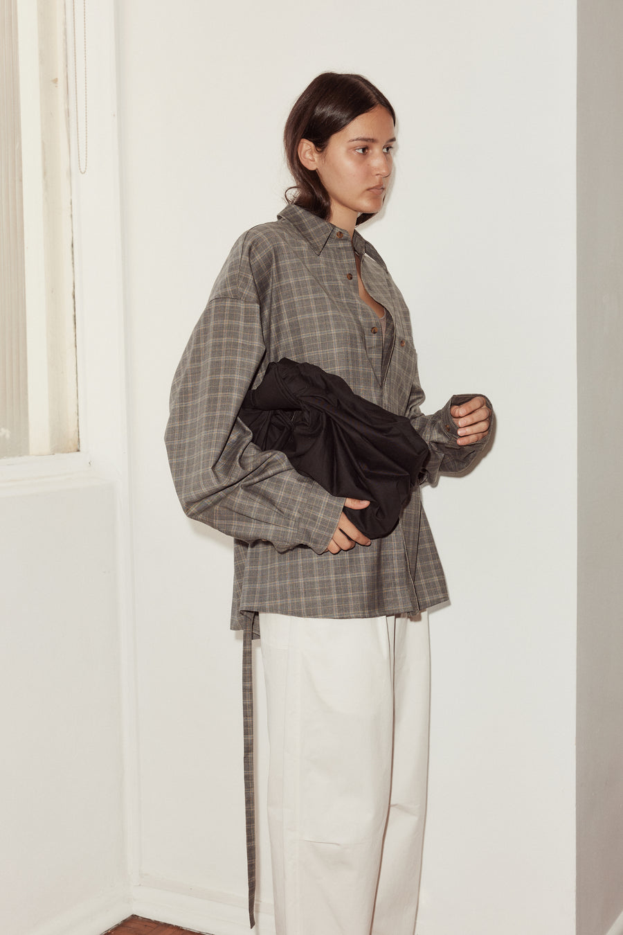 Mid shot of female model wearing the Wool Shirt in Everyday Check by Deiji Studios, holding the Bow Bag in black.