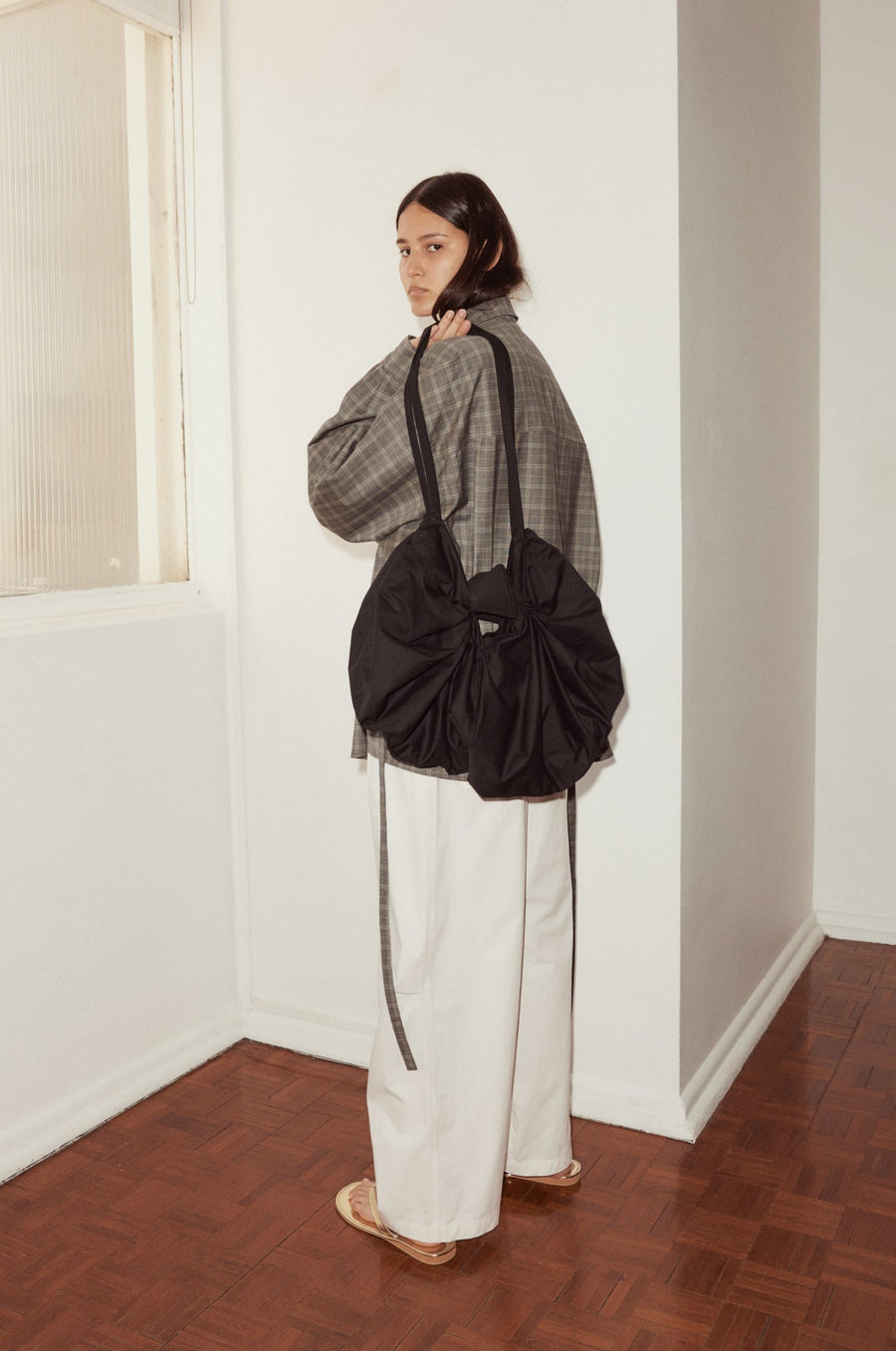 female model pictured with the Deiji Studios Bow Bag, a black organic cotton bag with subtle lustre in the shape of a ribbon bow, with long shoulder straps
