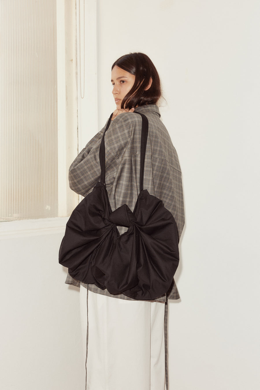 female model pictured with the Deiji Studios Bow Bag, a black organic cotton bag with subtle lustre in the shape of a ribbon bow, with long shoulder straps