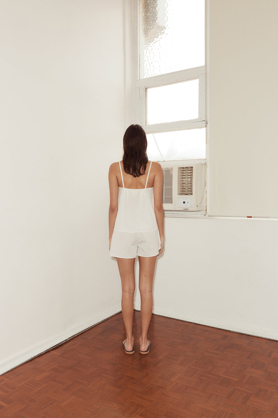 Back shot of female model wearing the Pleat Set in White, features double pleated tucks at back, thin straps and pull on shorts.