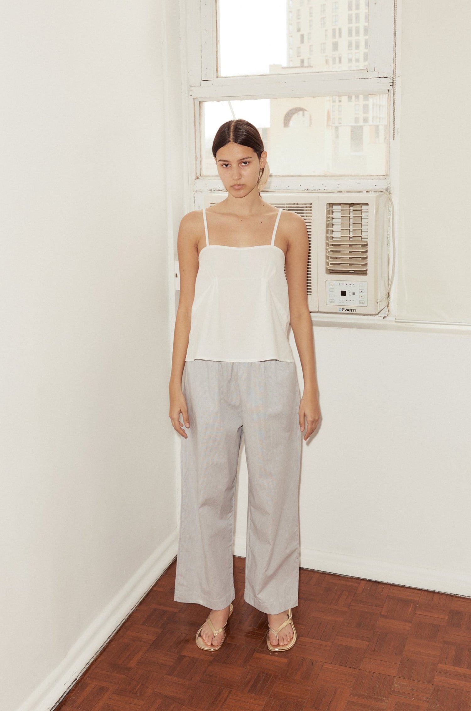 female model wears the Deiji Studios Ease Trouser in Dream Stripe, a soft blue micro stripe trouser in organic cotton poplin. Features side pockets, a relaxed leg and soft elastic waist. Styled with the Deiji Studios Pleat Top in white.