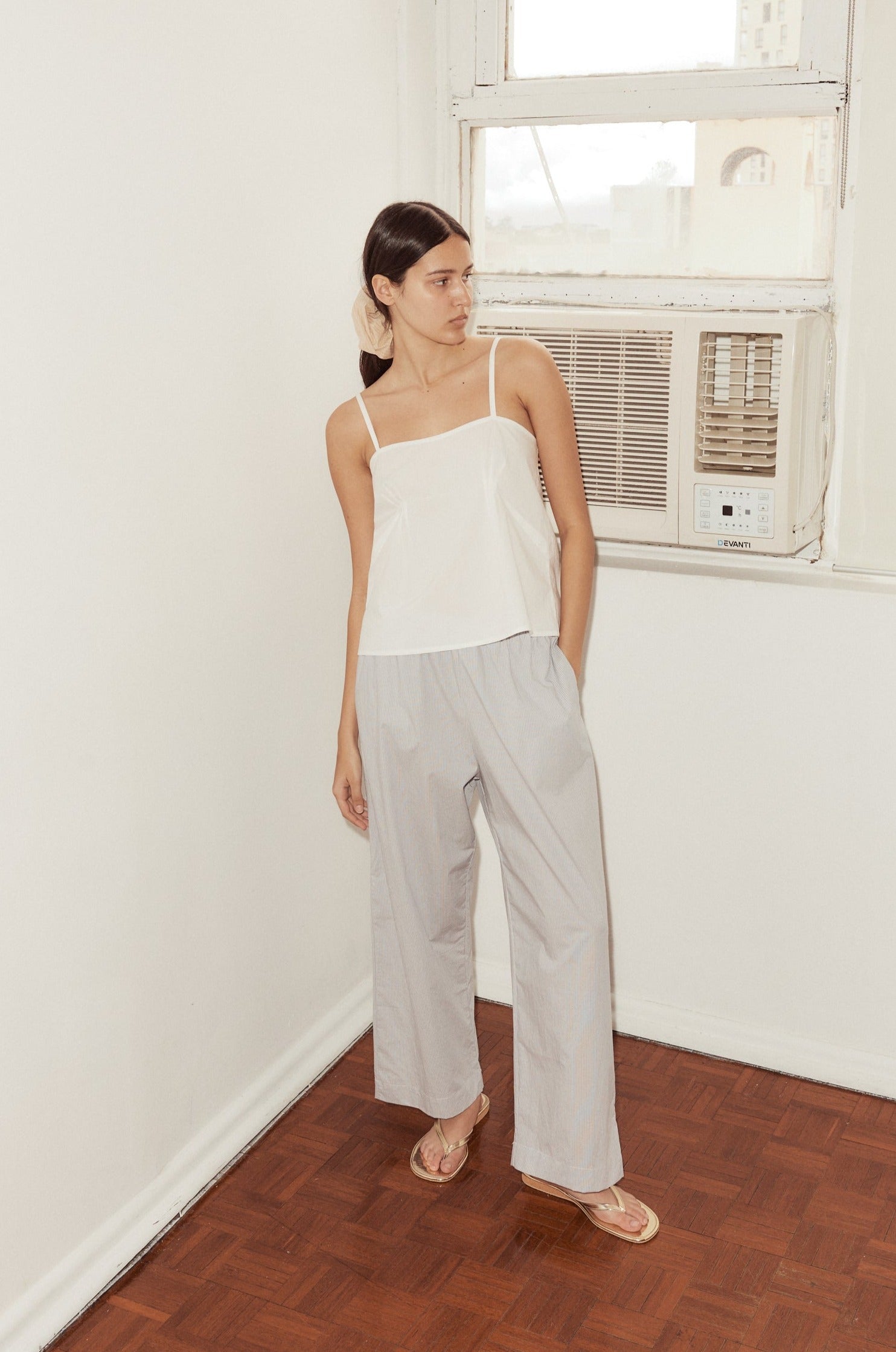 Mid shot of female model putting hand in pocket of Ease Trousers in Dream Stripe, styled with the Pleat Top in white.