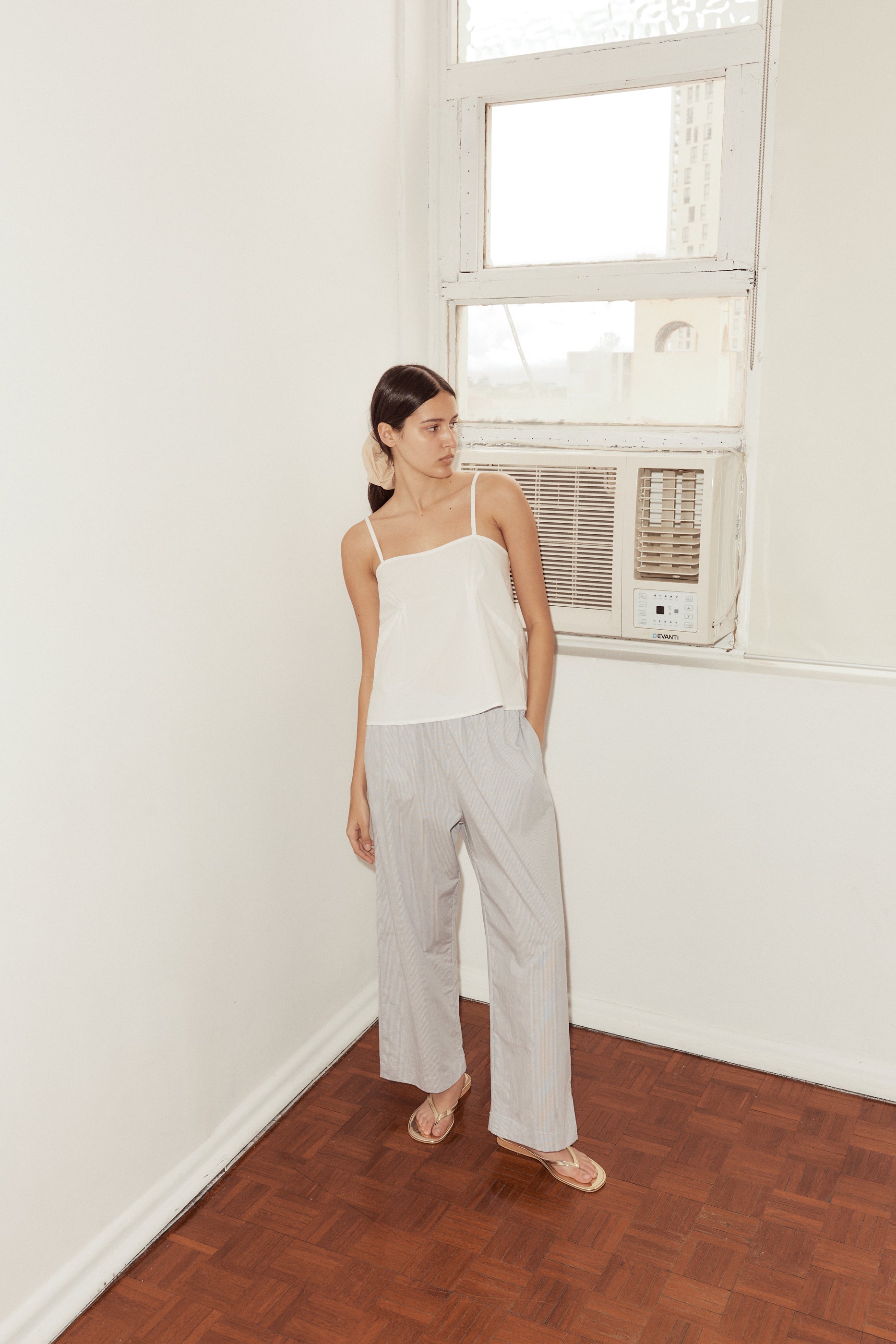 female model wears the Deiji Studios Ease Trouser in Dream Stripe, a soft blue micro stripe trouser in organic cotton poplin. Features side pockets, a relaxed leg and soft elastic waist. Styled with the Deiji Studios Pleat Top in white.