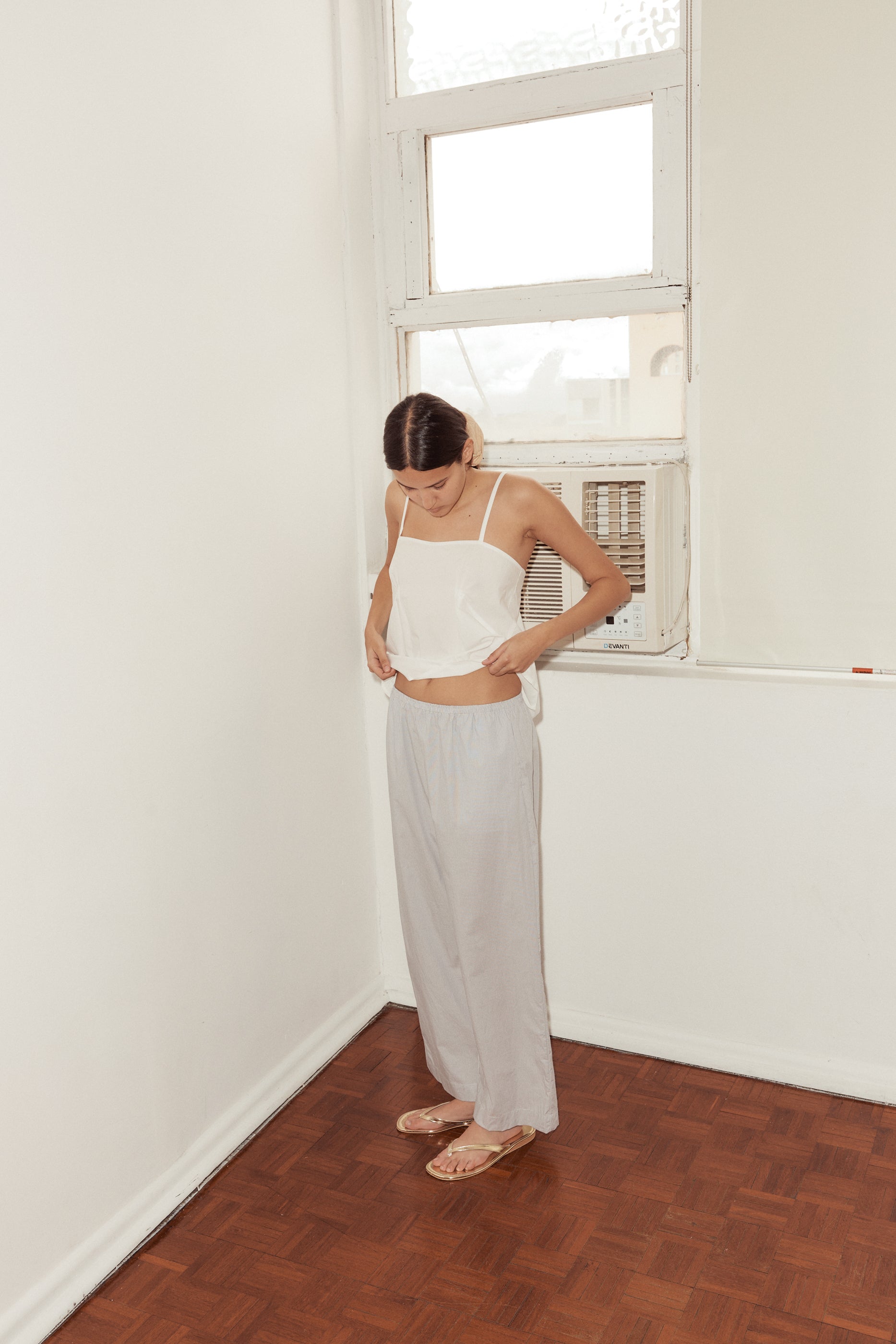 Female model lifts hem of Pleat Top in white to show soft elastic gathered waist of ease trouser in Dream Stripe.