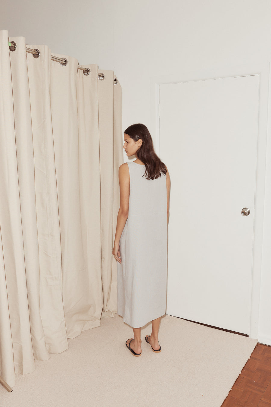 Back shot of female model wearing the Tuck Tie Dress by Deiji Studios in Dream Stripe. Dress features long simple back in mid length.