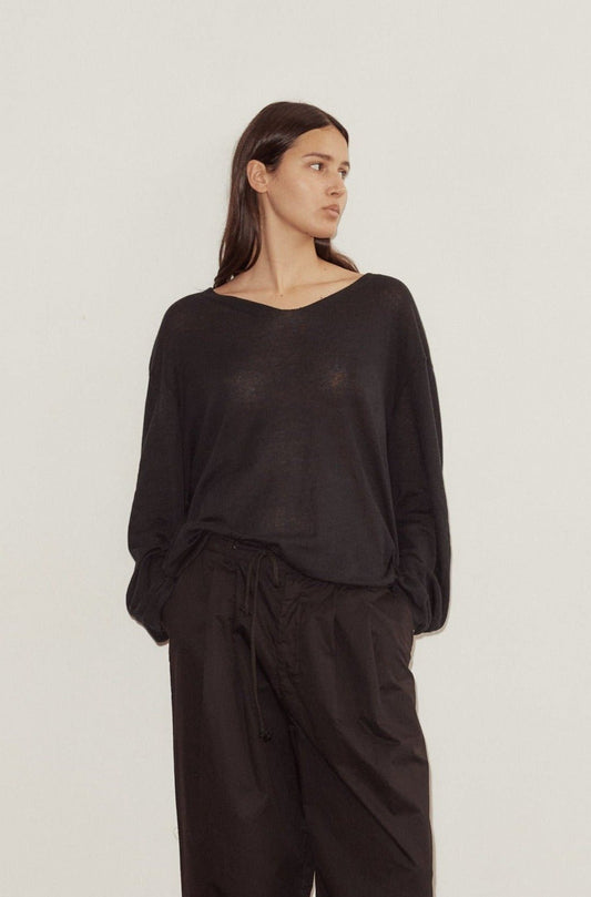 female model wears Deiji Studios loose long sleeve knitted top in black. A loose, open weave top with a soft v neck and elongated sleeves. Styled with the Deiji Studios Cotton Pant in black.