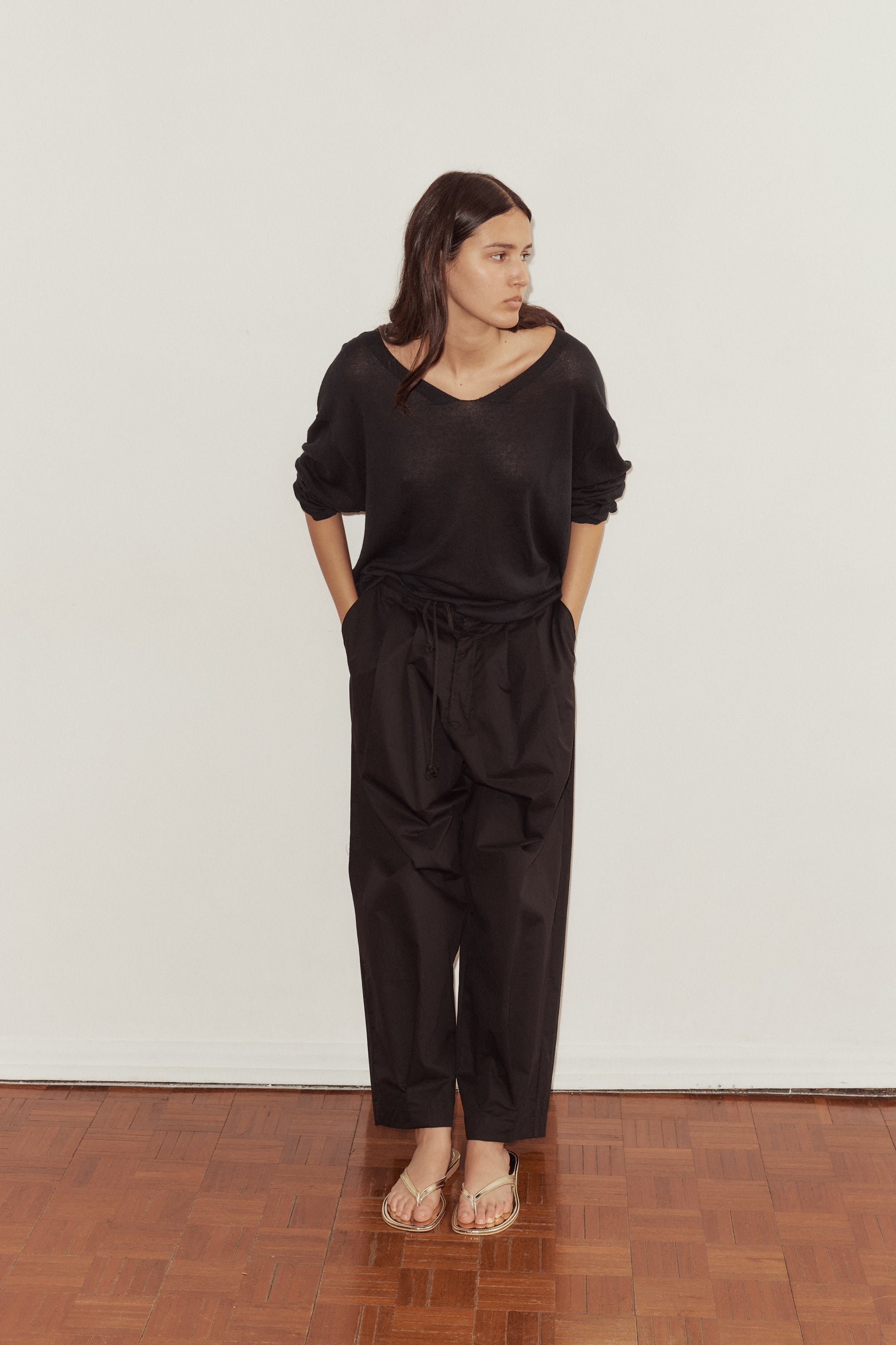 female model puts hands in pockets of the Deiji Studios Cotton Pant in black, a tailored trouser style pant with a relaxed leg. Styled with the Deiji Studios loose long sleeve knitted top in black.