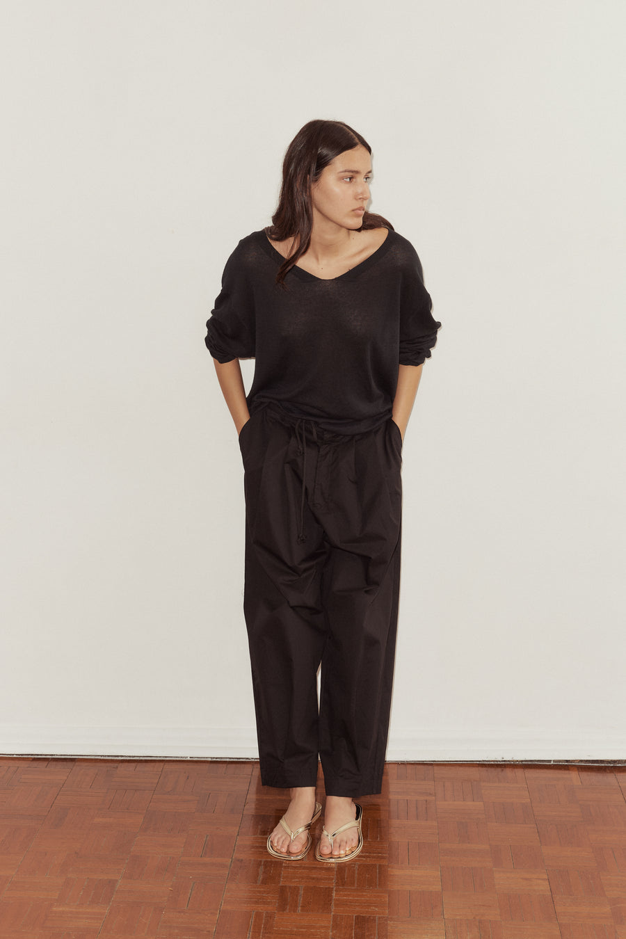female model puts hands in pockets of the Deiji Studios Cotton Pant in black, a tailored trouser style pant with a relaxed leg. Styled with the Deiji Studios loose long sleeve knitted top in black.