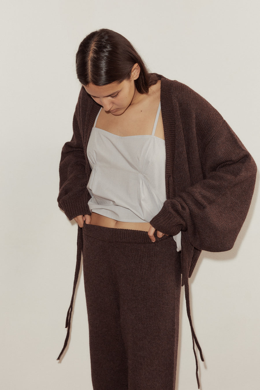 Close up shot of female model wearing the Two Tie Cardigan and Straight Knit Pant in Plum, styled with the Pleat Top in Dream Stripe. Pants show soft wide elastic waistband.