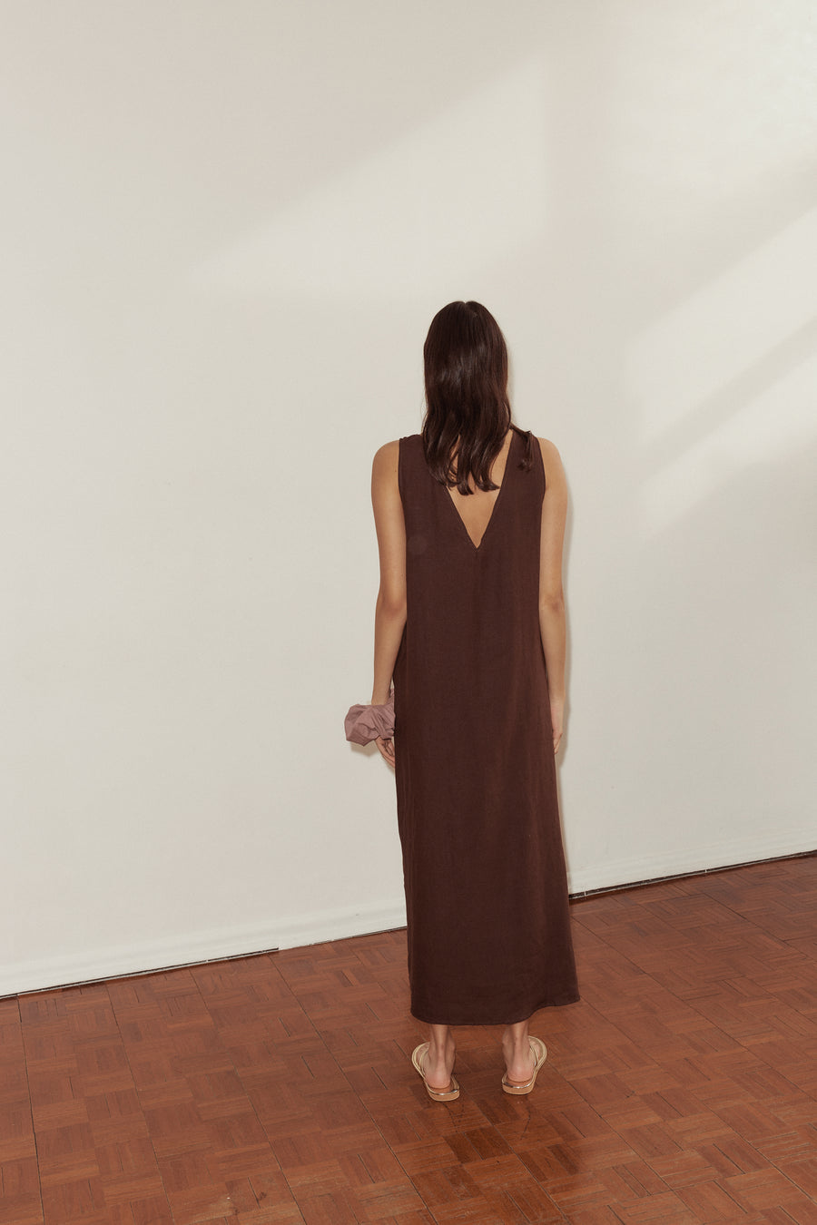 back shot of female model wearing the Keyhole Dress by Deiji Studios in burgundy linen. Features a v backline and full length. Styled with Deiji Studios scrunchie in lavender.
