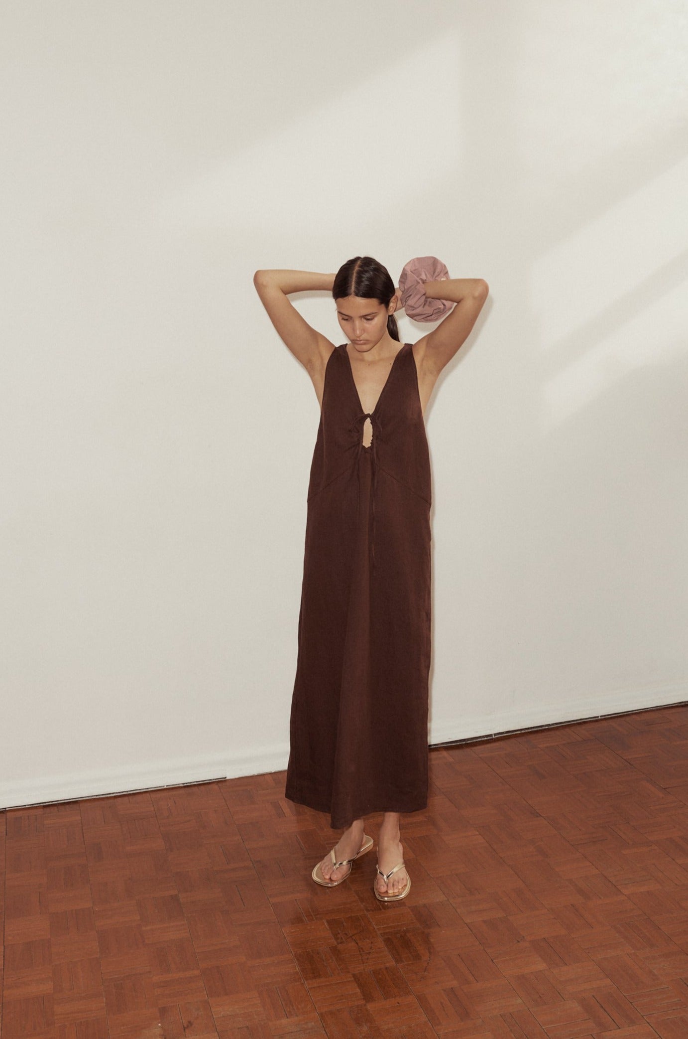 female model wears the Keyhole Dress by Deiji Studios in burgundy linen. Features a full length, seam detail, flattering v neckline and drawcord keyhole detail at bust. Styled with Deiji Studios scrunchie in Lavender worn on wrist.