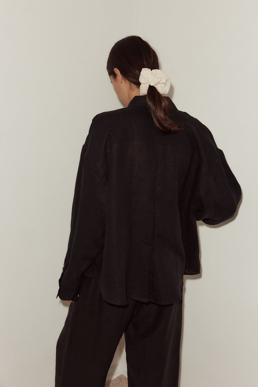 Back shot of female model wearing the tack Set by Deiji Studios in black. Shirt featured dropped shoulder and dropped back yoke for a relaxed look.
