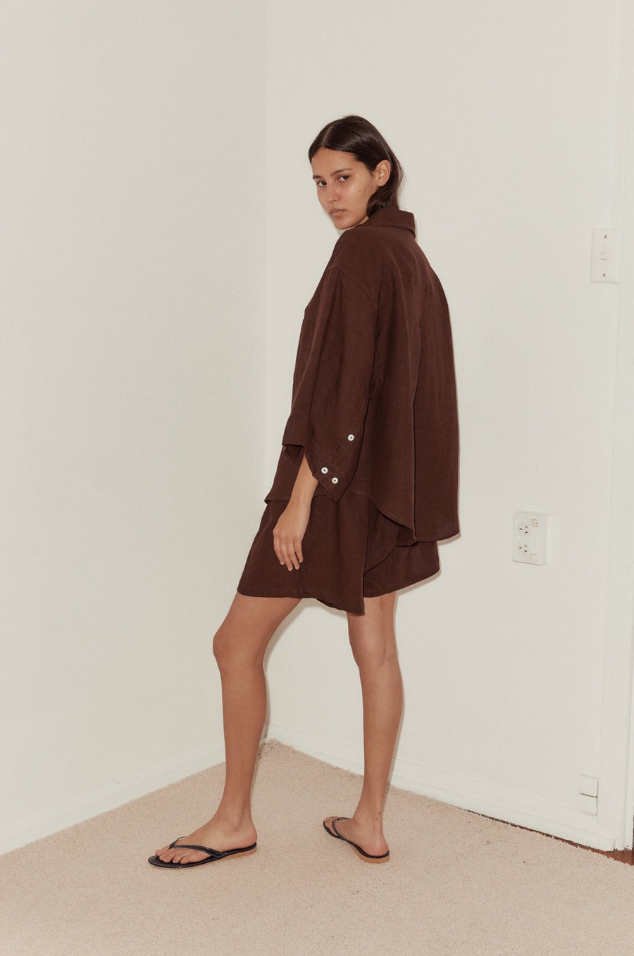 mid shot of female model wearing a burgundy Deiji Studios linen set, features an oversized shirt, button cuff and relaxed shorts