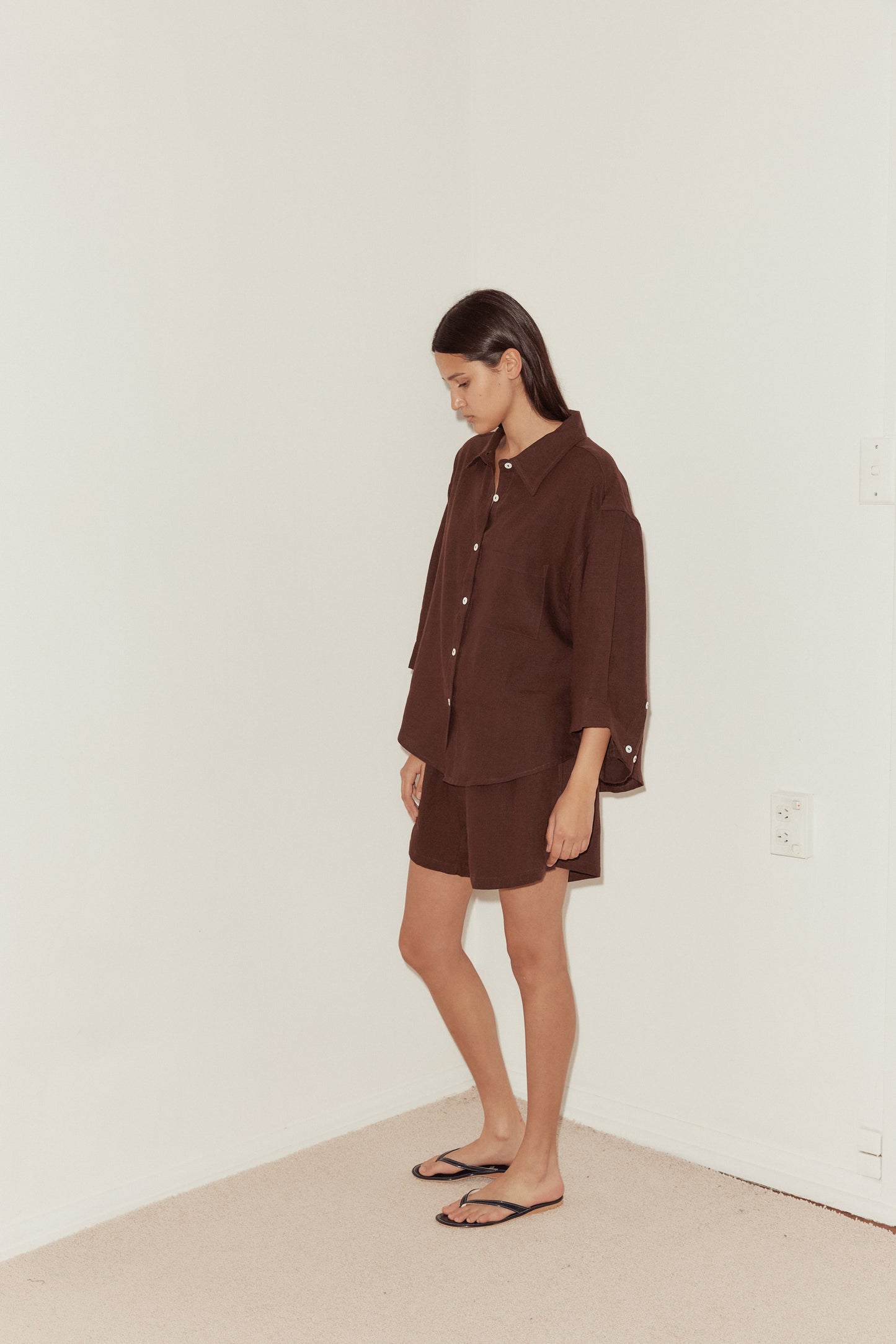 mid shot of a female model wearing a burgundy Deiji Studios linen set, features an oversized button down shirt and relaxed boxer shorts