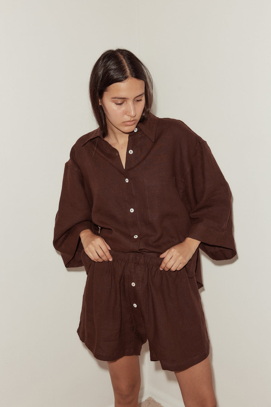 close up of a female model wearing a burgundy Deiji Studios linen set, features an oversized button down shirt and relaxed boxer shorts