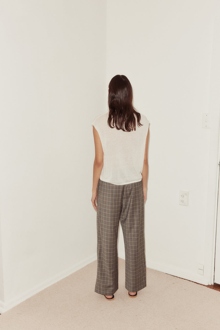 Back side shot of female model wearing the Tailored Pants in Everyday Check styled with the Loose Knitted Vest in white. Pant features relaxed leg in full length.