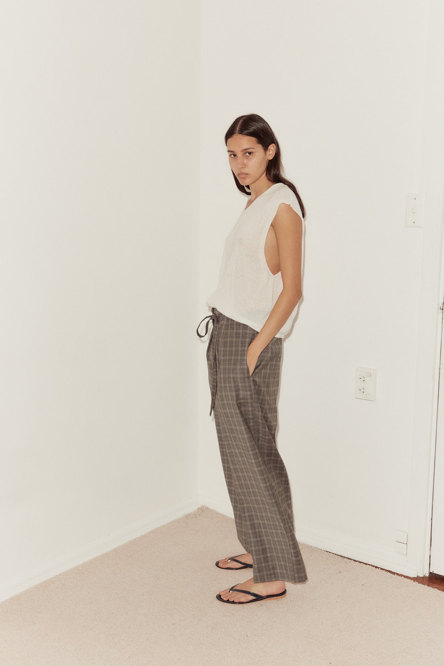 Mid side shot of female model wearing the Tailored Pants in Everyday Check styled with the Loose Knitted Vest in white. Pant features relaxed leg with side pockets.