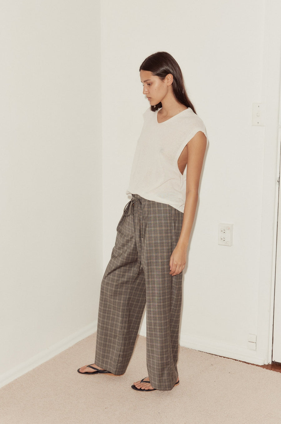 Mid shot of female model wearing the Tailored Pants in Everyday Check styled with the Loose Knitted Vest in white. Pant features relaxed wide leg with self fabric tie at waist opening.