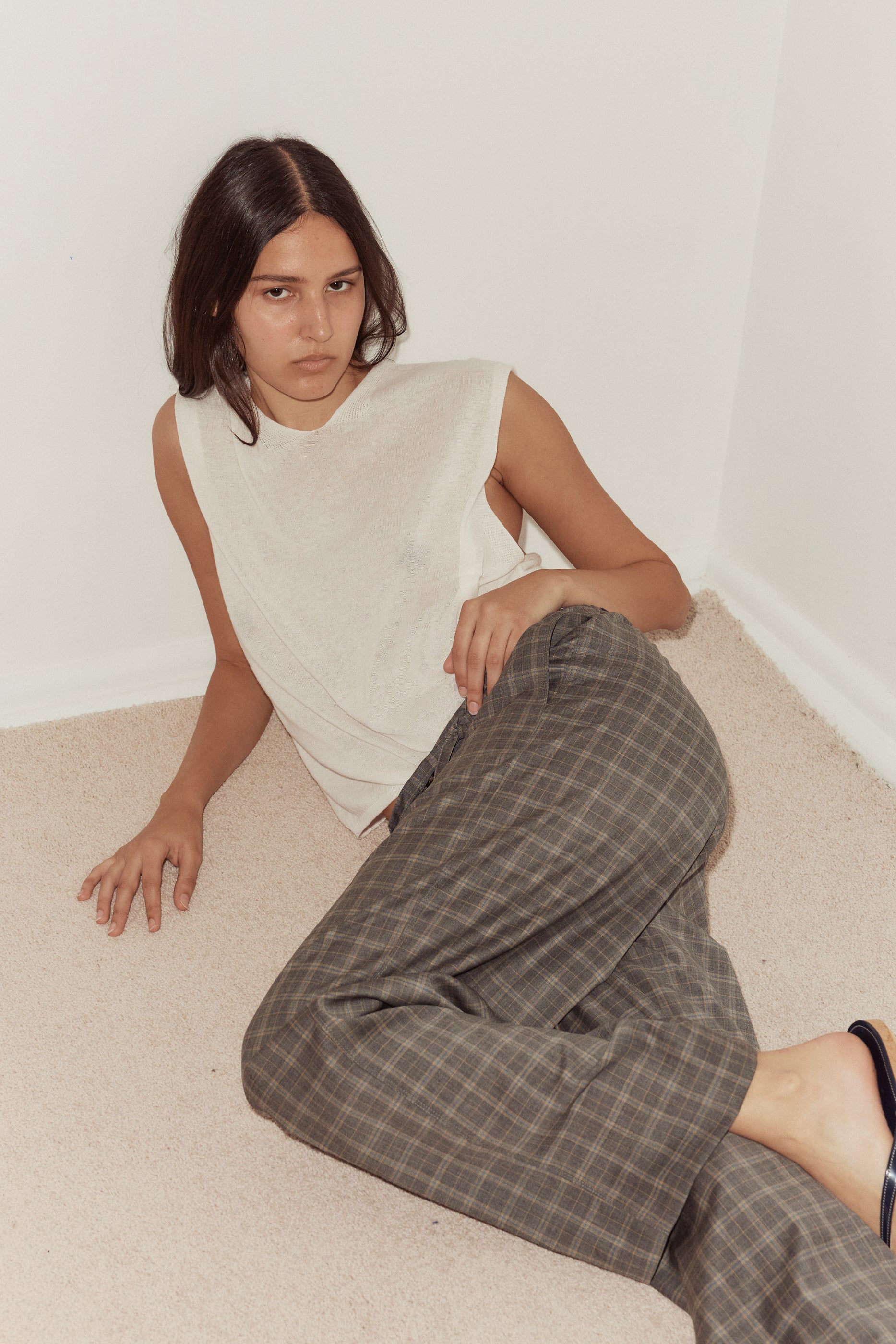 High angle shot of female model wearing the loose knitted vest in white by Deiji Studios. Lightweight knit vest with soft high v neckline in full length. Styled with the Everyday Pant by Deiji Studios in Wool Check.