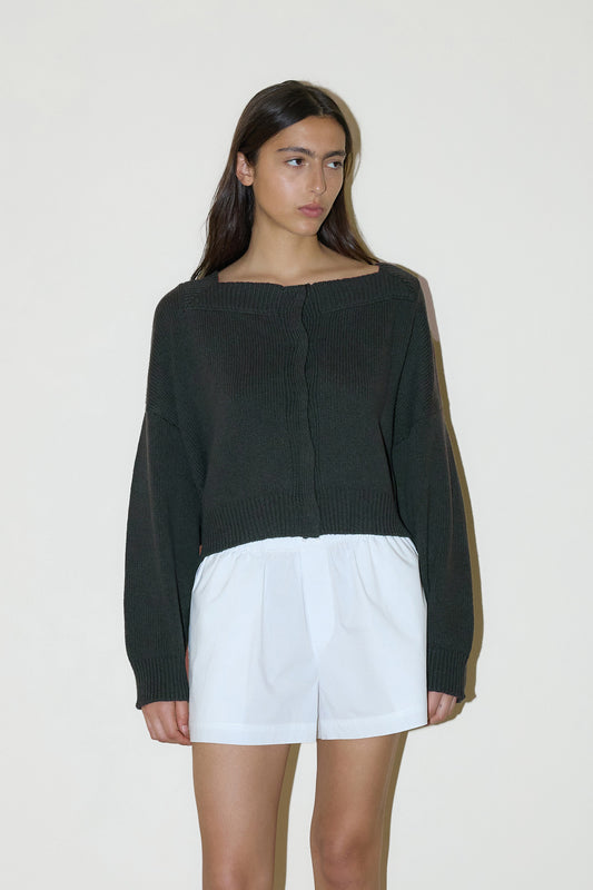 dark haired female model wears a forest green cropped, square-neck cardigan featuring snap button closure at front designed with a raised neckline for added structure and ribbed detailing at the cuffs and hem, paired with white easy pull-on boxer short designed to fit mid-rise, features a gathered elastic waistline with double button detailing.