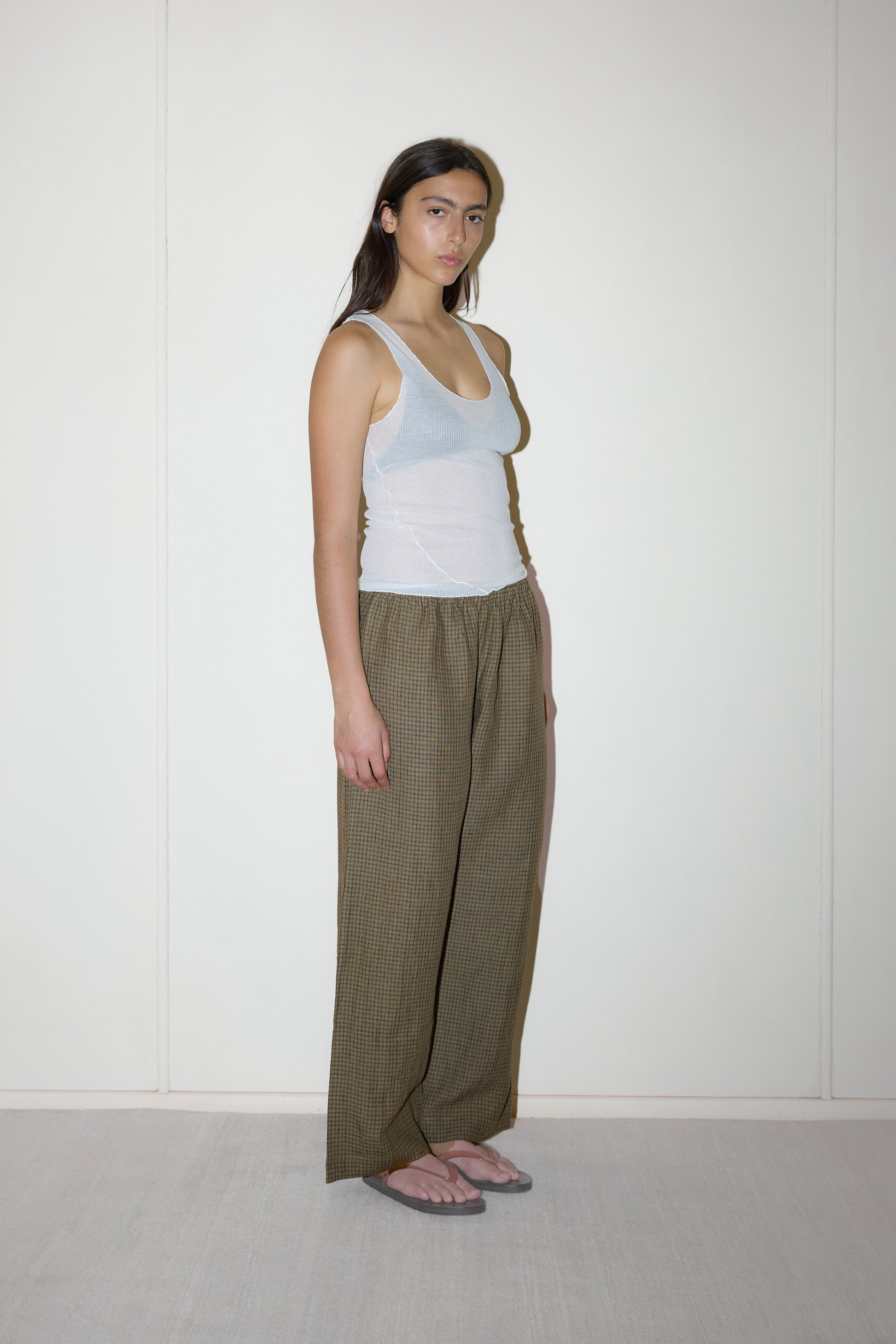 dark haired female model wears a brown and black gingham check printed pant full length relaxed pant features a soft minimal elastic waist with side seam pockets in a straight leg, paired with a knitted sheer tank in off-white 