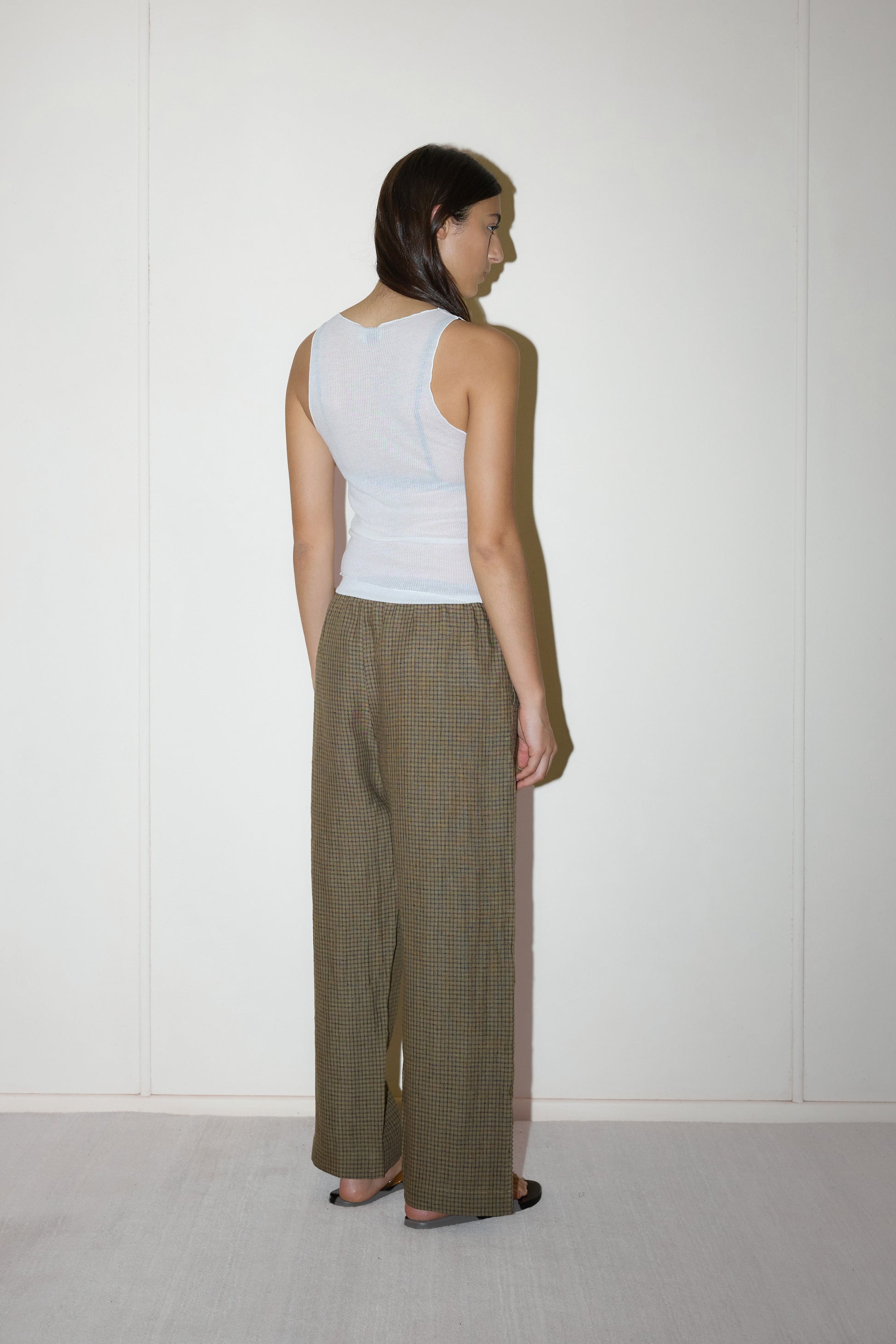 dark haired female model wears a brown and black gingham check printed pant full length relaxed pant features a soft minimal elastic waist with side seam pockets in a straight leg, paired with a knitted sheer tank in off-white 