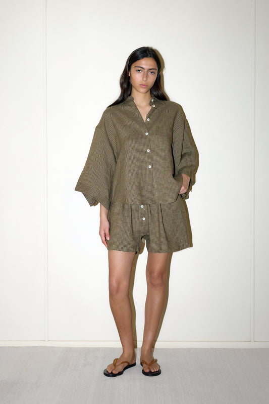 dark haired female model wears a brown and black gingham print shirt and short set in an oversized box fit linen shirt with wide arms and a front pocket designed to sit mid rise, the loose fitting boxer style shorts have a faux button down fly and an elastic waist for extra comfort