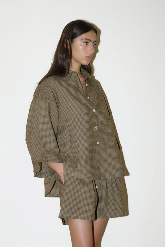 dark haired female model wears a brown and black gingham print shirt and short set in an oversized box fit linen shirt with wide arms and a front pocket designed to sit mid rise, the loose fitting boxer style shorts have a faux button down fly and an elastic waist for extra comfort